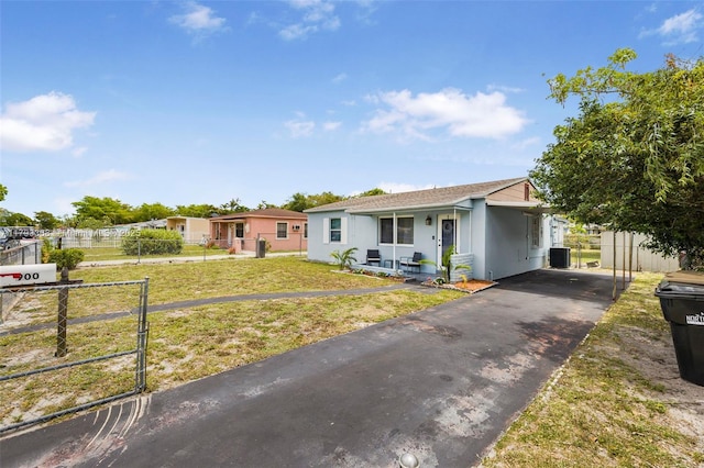 ranch-style home with covered porch, a front yard, central AC unit, fence, and aphalt driveway