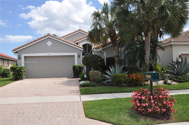 mediterranean / spanish home featuring decorative driveway, an attached garage, a tile roof, and stucco siding