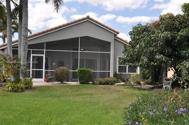 back of property featuring a lawn, stucco siding, a sunroom, and a tile roof