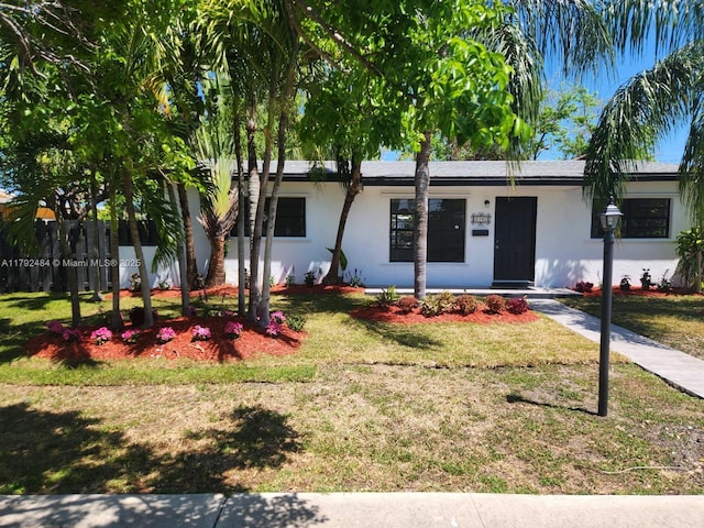 ranch-style home with fence, covered porch, stucco siding, and a front lawn