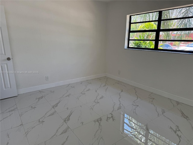 unfurnished room featuring baseboards, marble finish floor, and a wealth of natural light