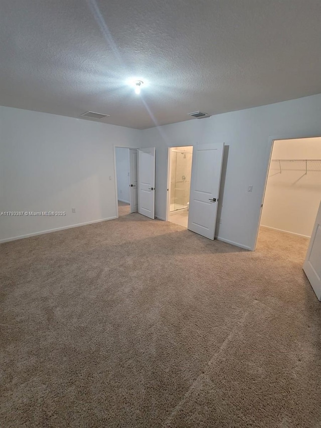 unfurnished bedroom featuring a textured ceiling, carpet, baseboards, a spacious closet, and visible vents