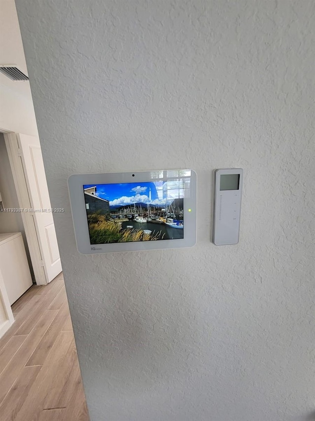 room details featuring a textured wall, visible vents, and wood finished floors