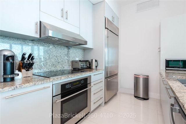 950 Brickell Bay Dr Unit 4710, Miami, FL 33131 - kitchen with stainless steel appliances, wall chimney exhaust hood, tasteful backsplash, white cabinets, and light stone counters