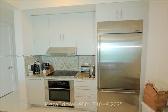 950 Brickell Bay Dr Unit 4710, Miami, FL 33131 - kitchen featuring backsplash, appliances with stainless steel finishes, light stone counters, white cabinets, and extractor fan