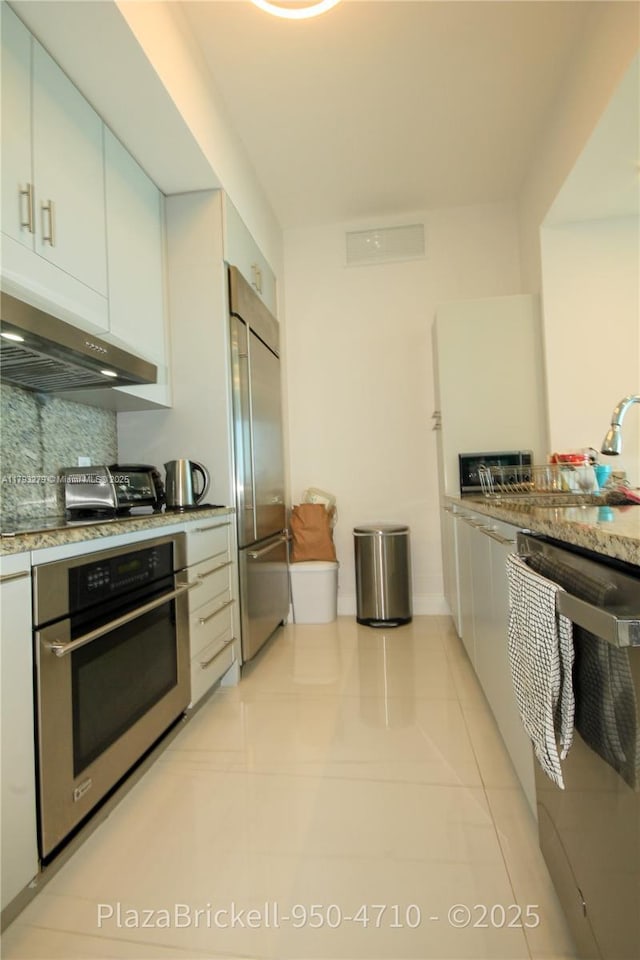950 Brickell Bay Dr Unit 4710, Miami, FL 33131 - kitchen featuring appliances with stainless steel finishes, backsplash, light tile patterned floors, a toaster, and under cabinet range hood