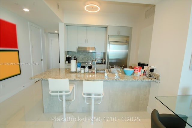 950 Brickell Bay Dr Unit 4710, Miami, FL 33131 - kitchen featuring wall chimney range hood, a sink, light stone counters, a peninsula, and stainless steel built in refrigerator