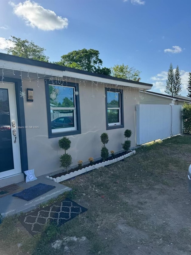 view of side of home with stucco siding and fence