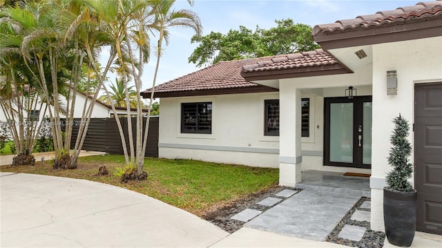 doorway to property featuring stucco siding, a tiled roof, and fence