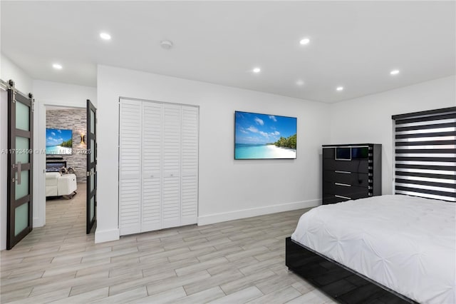 bedroom featuring a closet, baseboards, light wood-style floors, recessed lighting, and a barn door