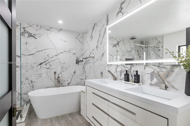 full bath featuring double vanity, tile walls, a soaking tub, a sink, and a marble finish shower