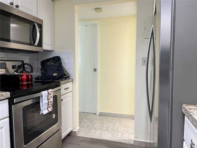 2655 Collins Ave Unit 1405, Miami Beach, FL 33140 - kitchen with backsplash, appliances with stainless steel finishes, light stone countertops, baseboards, and white cabinetry