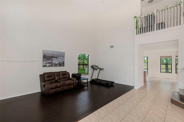 workout room with baseboards, visible vents, light wood-type flooring, and a towering ceiling