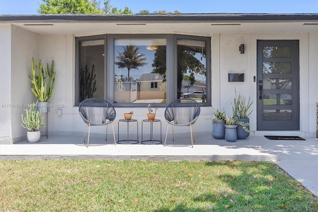 view of exterior entry with stucco siding and a yard