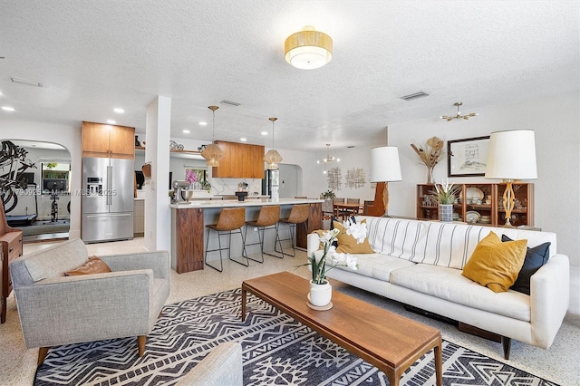 living room with an inviting chandelier, arched walkways, a textured ceiling, recessed lighting, and visible vents