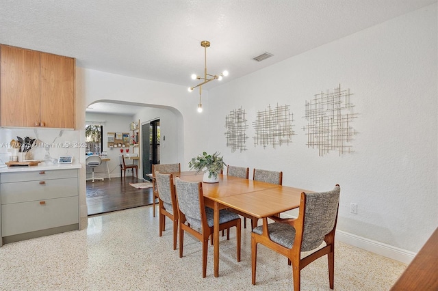 dining space featuring visible vents, arched walkways, light speckled floor, baseboards, and a notable chandelier