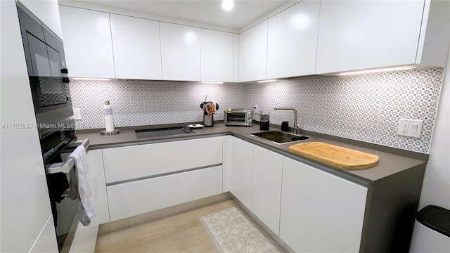 kitchen with dark countertops, a sink, white cabinetry, decorative backsplash, and a toaster