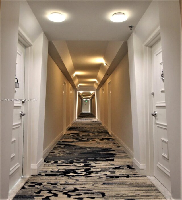 corridor featuring baseboards, vaulted ceiling, and carpet