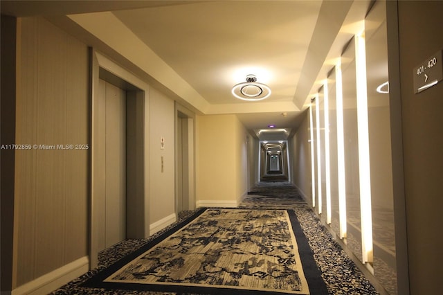 hall featuring baseboards, elevator, and a raised ceiling