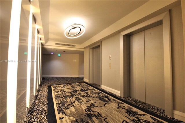 hallway with visible vents, baseboards, and elevator