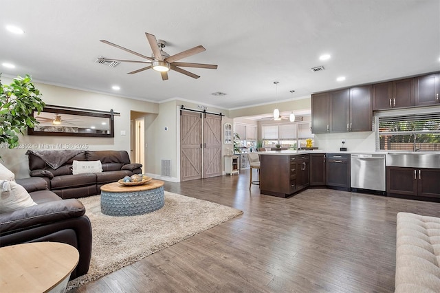 living area with a ceiling fan, visible vents, a barn door, and ornamental molding