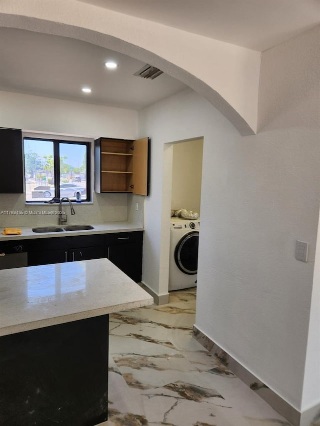 kitchen with washer / clothes dryer, visible vents, arched walkways, a sink, and dark cabinets