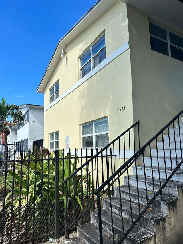 view of side of property with fence, stairs, and stucco siding