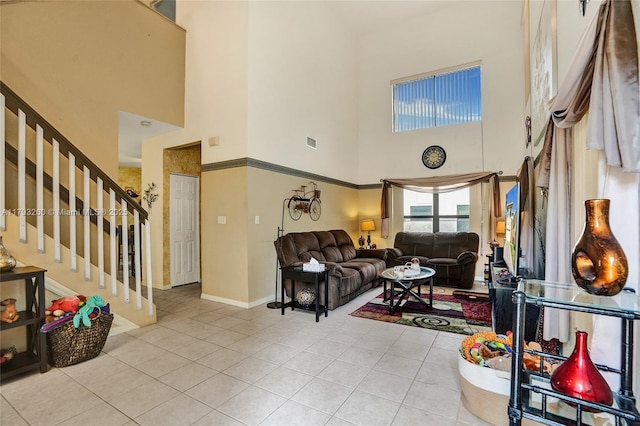 tiled living area with baseboards, visible vents, stairway, and a towering ceiling