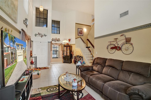 tiled living room featuring visible vents, a wealth of natural light, stairway, and a towering ceiling