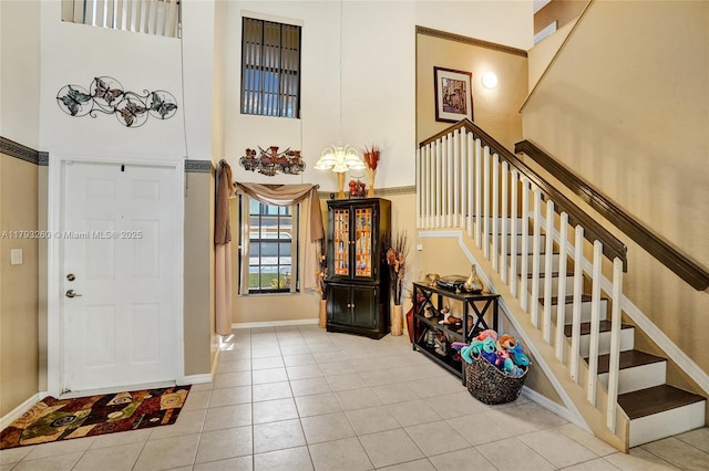 tiled entrance foyer with stairway, baseboards, and a towering ceiling
