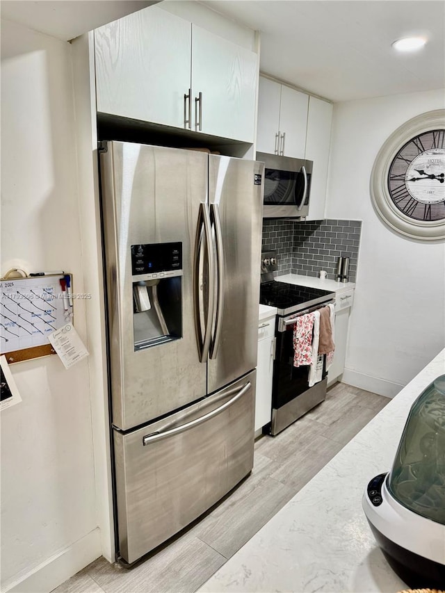 kitchen with light wood-type flooring, light countertops, appliances with stainless steel finishes, and backsplash