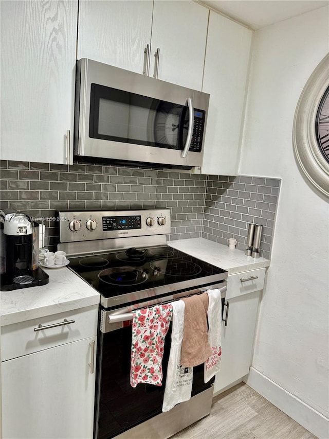 kitchen with light wood-style floors, appliances with stainless steel finishes, backsplash, and white cabinets