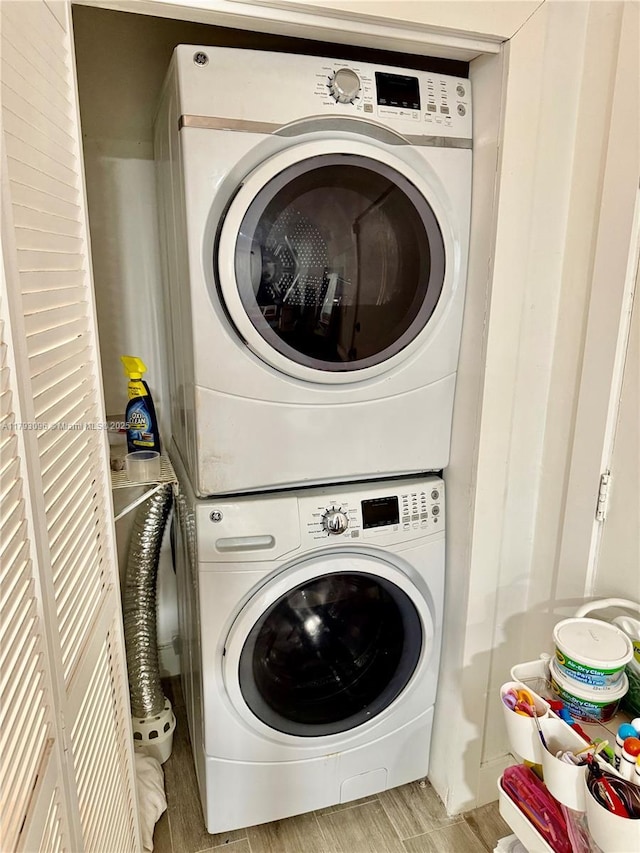 clothes washing area featuring laundry area, stacked washer and dryer, and wood finished floors
