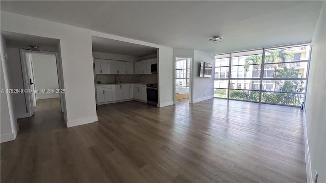 unfurnished living room with a sink, baseboards, a wall of windows, and dark wood-style flooring