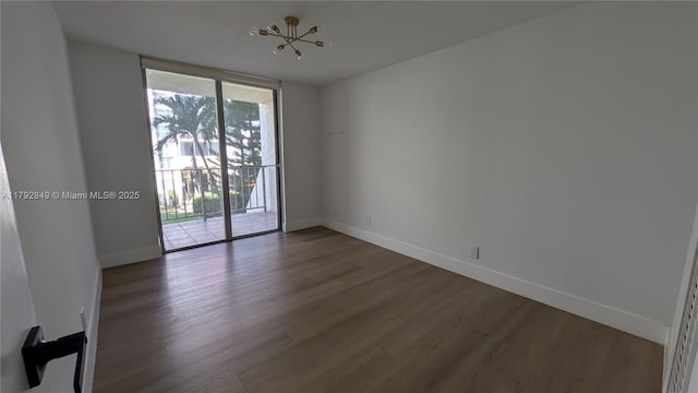 empty room with baseboards, a chandelier, and wood finished floors