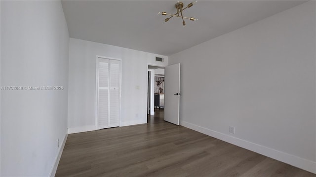 unfurnished bedroom with a notable chandelier, baseboards, wood finished floors, visible vents, and a closet