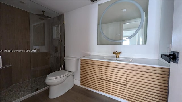 full bathroom featuring vanity, wood finished floors, a tile shower, and toilet