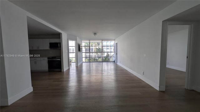 unfurnished living room with baseboards, a wall of windows, and dark wood-type flooring