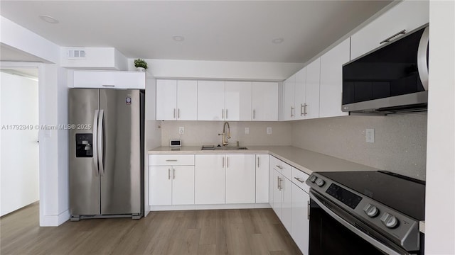 kitchen with decorative backsplash, light wood-type flooring, light countertops, a sink, and stainless steel appliances