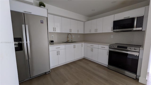 kitchen with appliances with stainless steel finishes, wood finished floors, a sink, light countertops, and white cabinetry