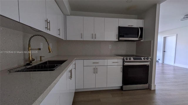 kitchen featuring backsplash, a sink, white cabinets, light wood finished floors, and stainless steel appliances