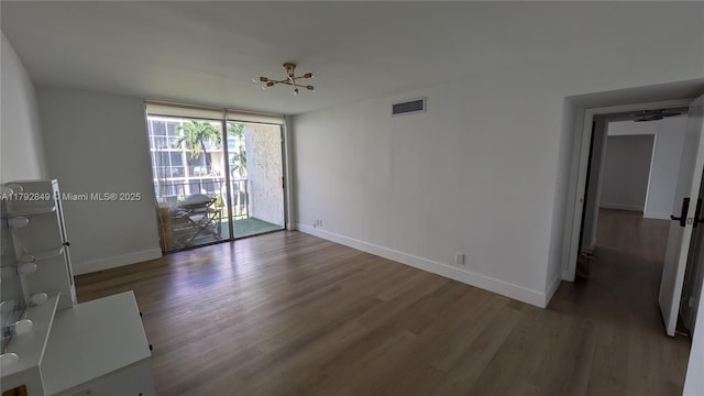 empty room with a wall of windows, baseboards, wood finished floors, and visible vents