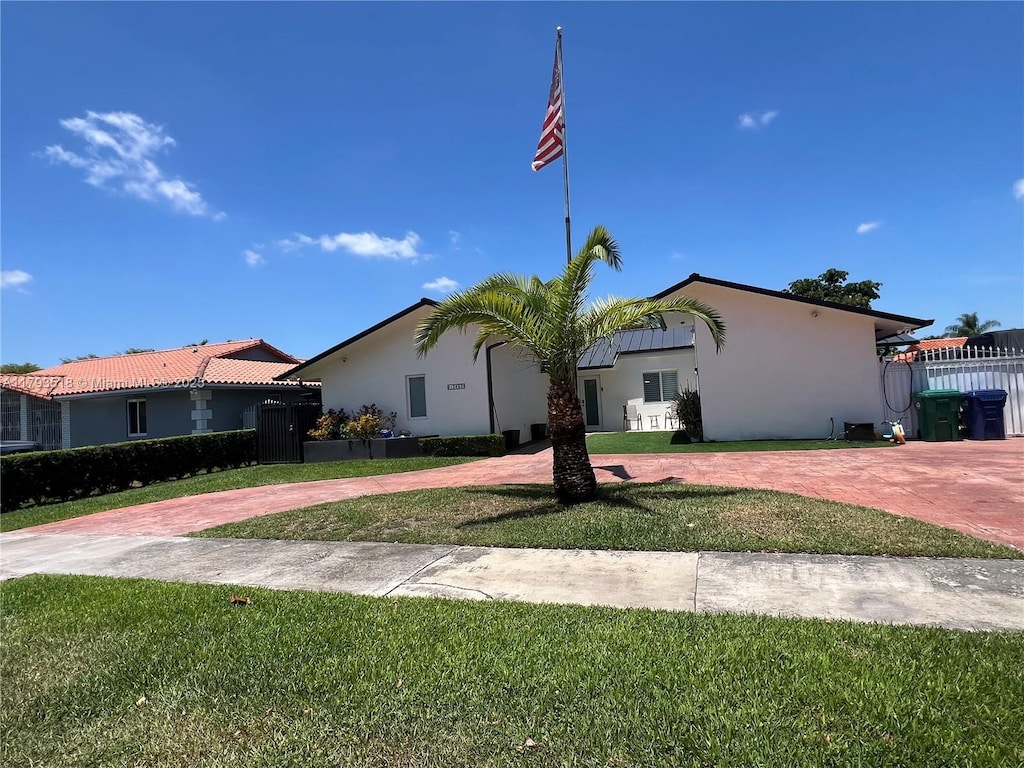 view of front of house with decorative driveway, a front lawn, stucco siding, and fence