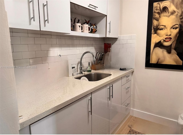kitchen with backsplash, open shelves, light stone countertops, a sink, and white cabinets