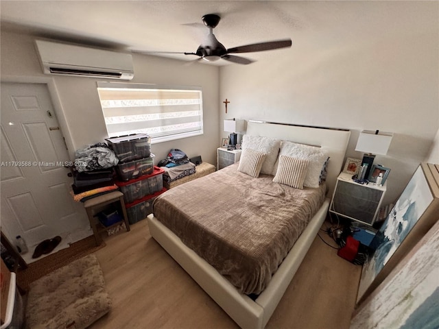 bedroom with ceiling fan, a wall unit AC, and wood finished floors