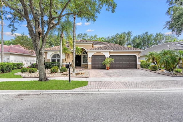 mediterranean / spanish house featuring stucco siding, an attached garage, driveway, and a tile roof