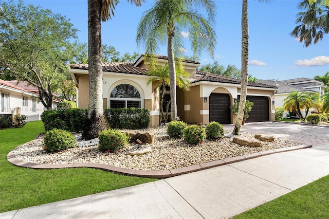 mediterranean / spanish-style home featuring a front lawn, a garage, stucco siding, a tiled roof, and driveway