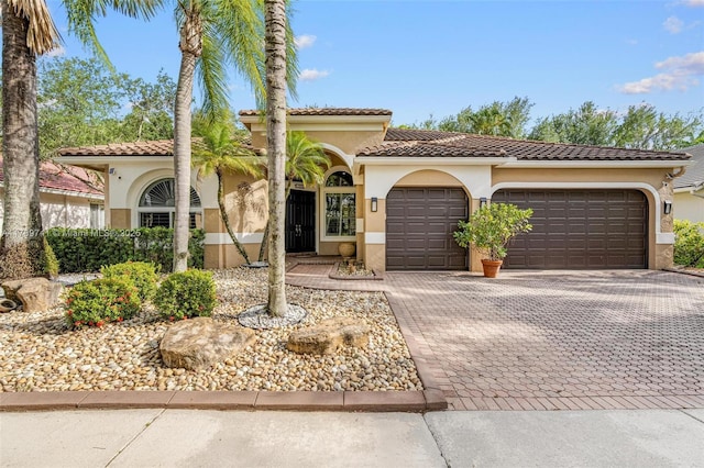 mediterranean / spanish-style home with a garage, stucco siding, and decorative driveway