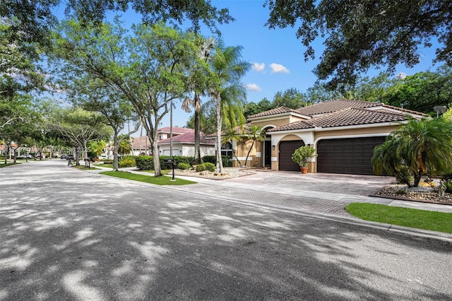 view of front facade featuring an attached garage, driveway, a tile roof, and stucco siding