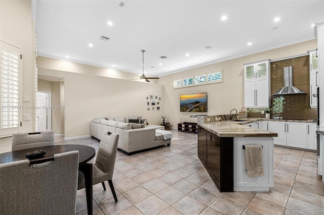 kitchen featuring crown molding, open floor plan, a peninsula, and wall chimney range hood